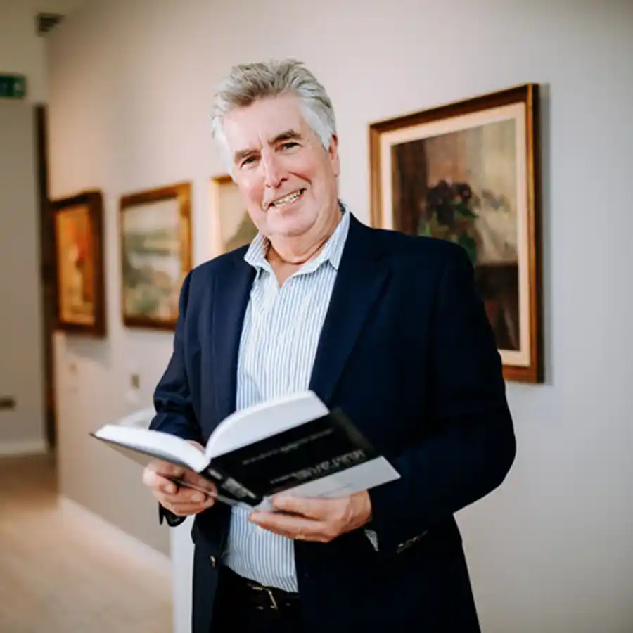 Dr Robb Robinson of Hull University, holding a book with a gallery backdrop.